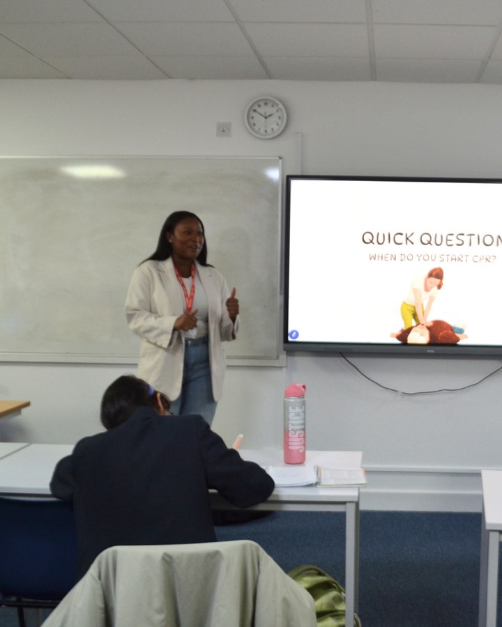 Dr Emefa Vondee teaching a class, standing beside a screen reading Quick question: when do you start CPR?